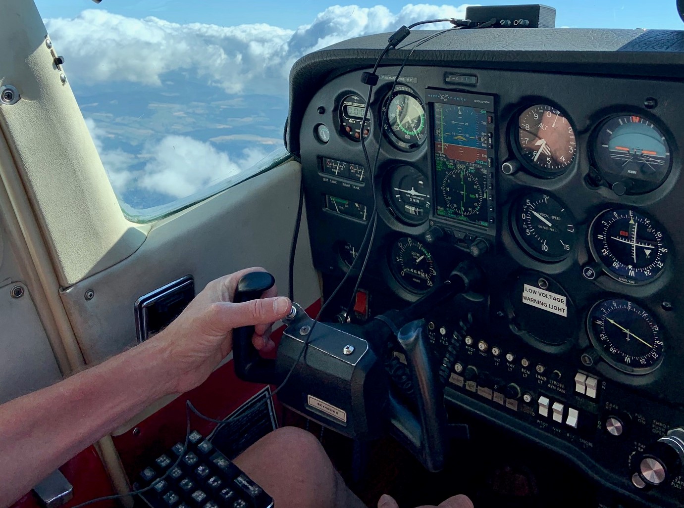 Unité secondaire  du soundflyer installée, en vol : sur un fond de nuage, deux mains manient les commandes, devant le tableau de bord