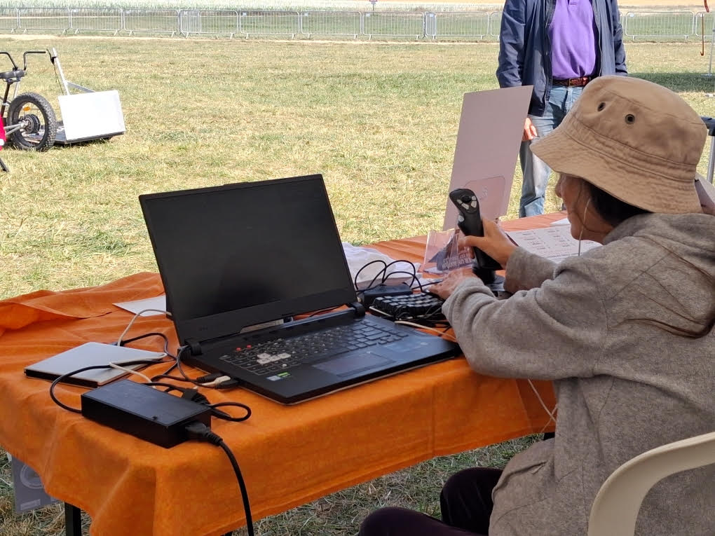 De dos, une de nos adhérentes est en train de pratiquer sur le simulateur de vol, sur le stand de l'association, face au terrain de vol engazonné.