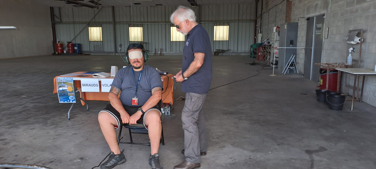 Au stand des Mirauds volants, un visiteur, sous le bandeau, teste l'appareillage du soundflyer dans un grand hangar. 
